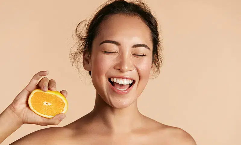Femme souriante tenant une demi-orange, illustration de l’approche naturelle de Jade Mazère